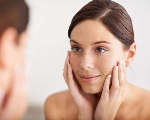 A young woman looking at her reflection in the mirror with her hands on her face