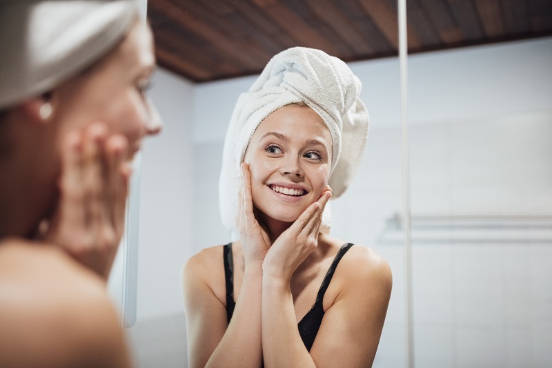 Girl with towel is looking in a mirror